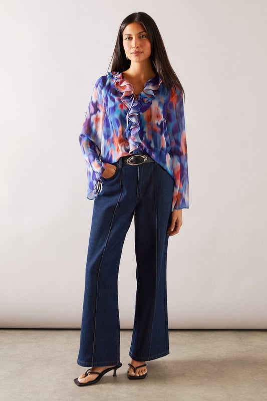 Elegant V-neckline with cascading ruffle detail for a feminine touch
        Flowing long sleeves with delicate tie cuffs for adjustable styling
        Lightweight, floaty fabric that drapes beautifully across the silhouette
        Versatile regular fit that flatters all body shapes
        Distinctive watercolour-inspired print that adds visual interest to any outfit
    
    This Wallis blouse combines sophisticated style with everyday comfort. The eye-catching ruffle detail creates a flattering vertical line while the tie feature adds a touch of refinement. Perfect for daytime occasions, style with wide-leg denim trousers and a statement belt for family gatherings or weekend brunches. The flowing sleeves create movement and balance the silhouette beautifully. For a more casual approach, pair with your favourite jeans and flat sandals for shopping trips or coffee dates. The versatile design transitions effortlessly from desk to dinner - simply swap your daytime accessories for more striking jewellery to refresh your look. This blouse offers the glamour and sophistication Wallis is known for whilst maintaining comfort for all-day wear.