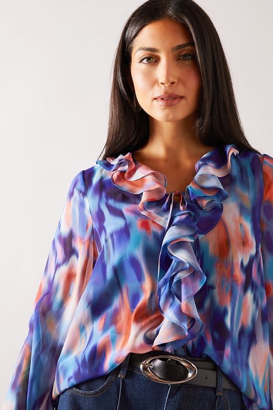 Elegant V-neckline with cascading ruffle detail for a feminine touch
        Flowing long sleeves with delicate tie cuffs for adjustable styling
        Lightweight, floaty fabric that drapes beautifully across the silhouette
        Versatile regular fit that flatters all body shapes
        Distinctive watercolour-inspired print that adds visual interest to any outfit
    
    This Wallis blouse combines sophisticated style with everyday comfort. The eye-catching ruffle detail creates a flattering vertical line while the tie feature adds a touch of refinement. Perfect for daytime occasions, style with wide-leg denim trousers and a statement belt for family gatherings or weekend brunches. The flowing sleeves create movement and balance the silhouette beautifully. For a more casual approach, pair with your favourite jeans and flat sandals for shopping trips or coffee dates. The versatile design transitions effortlessly from desk to dinner - simply swap your daytime accessories for more striking jewellery to refresh your look. This blouse offers the glamour and sophistication Wallis is known for whilst maintaining comfort for all-day wear.