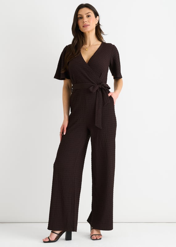 Verwen jezelf met luxe in onze Chocolate Textured Jersey Jumpsuit. Het wikkelontwerp voegt verfijning toe terwijl de wijde pijpen zorgen voor een flatterend silhouet. De getextureerde jersey stof voegt een vleugje elegantie toe. Deze jumpsuit is perfect voor elke gelegenheid en een must-have voor de modebewuste vrouw.