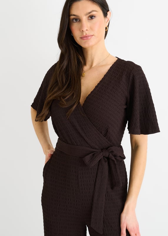 Verwen jezelf met luxe in onze Chocolate Textured Jersey Jumpsuit. Het wikkelontwerp voegt verfijning toe terwijl de wijde pijpen zorgen voor een flatterend silhouet. De getextureerde jersey stof voegt een vleugje elegantie toe. Deze jumpsuit is perfect voor elke gelegenheid en een must-have voor de modebewuste vrouw.