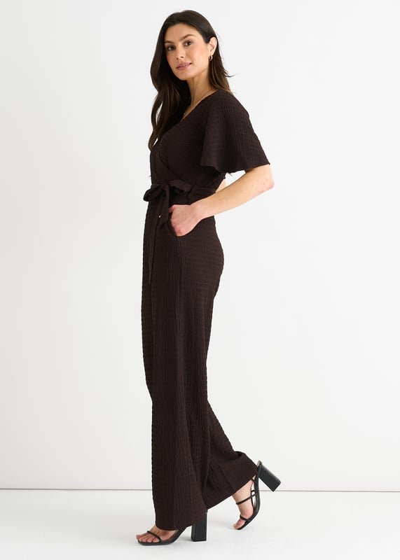 Verwen jezelf met luxe in onze Chocolate Textured Jersey Jumpsuit. Het wikkelontwerp voegt verfijning toe terwijl de wijde pijpen zorgen voor een flatterend silhouet. De getextureerde jersey stof voegt een vleugje elegantie toe. Deze jumpsuit is perfect voor elke gelegenheid en een must-have voor de modebewuste vrouw.