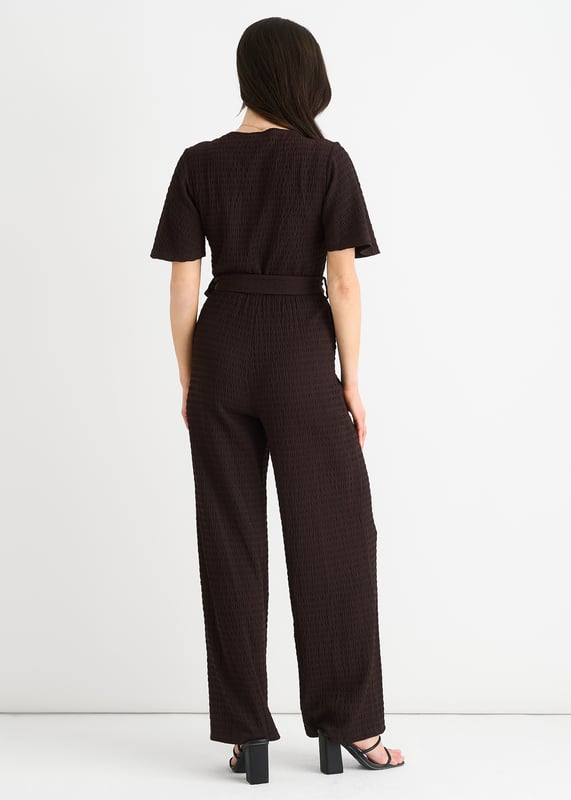 Verwen jezelf met luxe in onze Chocolate Textured Jersey Jumpsuit. Het wikkelontwerp voegt verfijning toe terwijl de wijde pijpen zorgen voor een flatterend silhouet. De getextureerde jersey stof voegt een vleugje elegantie toe. Deze jumpsuit is perfect voor elke gelegenheid en een must-have voor de modebewuste vrouw.