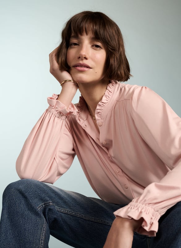 Description\nFits true to size, we suggest ordering your usual size.\nSima is a frill-adorned take on our best-selling Imken blouse. This feminine shirt features a relaxed collar with a ruffled trim - a detail that’s echoed in the elasticated cuffs. Cut from planet-conscious jersey for easy, all-day comfort, it’s a hard-working style to see you through work days and weekends.\n\nMade in Europe\nCrafted in LENZING™ ECOVERO™ jersey\nRelaxed fit\nGathered detail around the shoulders\n\n\nSustainable Attributes:\n Low Impact  Low Water Use Ethically made  Vegan   Low Carbon  \n\nDetails\nModel is 5'10 (177cm) and is wearing a UK 1095% LENZING™ ECOVERO™ Viscose, 5% ElastaneDelicate Machine Wash 30˚Product code: JB40007-PPKBack shoulder at neck to hem - 62cm (24 2/5)Sleeve length - 62cm (24 2/5)