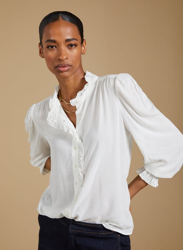 Description\nIf a feminine blouse is your thing, then you won’t be able to resist Aurora! This style is all you need to elevate a pair of jeans, thanks to the soft ruffle trim adorning the collar and placket. The fabric is special too: in a semi-sheer textured spot jacquard, proudly makes use of surplus fabric.\n\nMade in Europe\nCrafted in fine woven jacquard fabric\nButtons through\nElasticated cuffs\n¾ Length gathered sleeve detail\n\n\nSustainable Attributes:\n  Low Impact   Low Water Use  Ethically made  Low Carbon  \n\nDetails\nModel is 5'10 (177cm) and is wearing a UK 10100% ViscoseDry Clean Only Product code: SH40285-CREBack shoulder at neck to hem - 60cm (23 5/8)Sleeve length - 64cm (25 1/4)