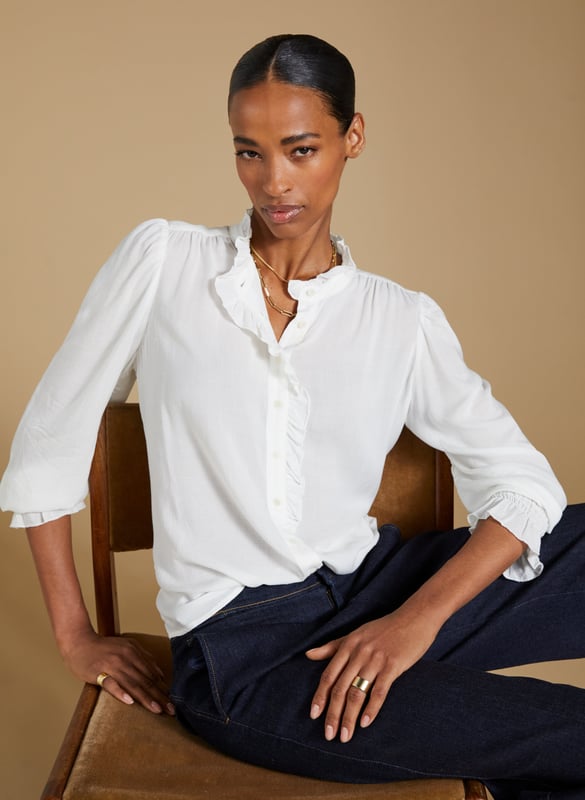 Description\nIf a feminine blouse is your thing, then you won’t be able to resist Aurora! This style is all you need to elevate a pair of jeans, thanks to the soft ruffle trim adorning the collar and placket. The fabric is special too: in a semi-sheer textured spot jacquard, proudly makes use of surplus fabric.\n\nMade in Europe\nCrafted in fine woven jacquard fabric\nButtons through\nElasticated cuffs\n¾ Length gathered sleeve detail\n\n\nSustainable Attributes:\n  Low Impact   Low Water Use  Ethically made  Low Carbon  \n\nDetails\nModel is 5'10 (177cm) and is wearing a UK 10100% ViscoseDry Clean Only Product code: SH40285-CREBack shoulder at neck to hem - 60cm (23 5/8)Sleeve length - 64cm (25 1/4)