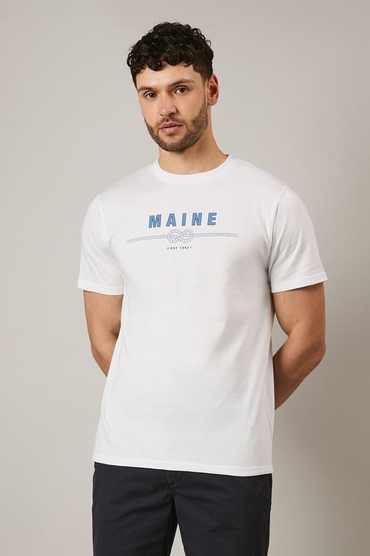 Soft jersey cotton t-shirt featuring the distinctive Maine rope graphic print
        Classic crew neckline with ribbed trim for a comfortable fit
        Short sleeves with clean-finished edges for everyday comfort
        Relaxed yet structured silhouette that maintains its shape throughout the day
        Versatile design that pairs effortlessly with both casual and smart-casual attire
    
    This Maine graphic t-shirt combines simplicity with subtle nautical flair, making it a wardrobe essential for the modern gent. The distinctive rope design adds character without overwhelming, perfect for those who appreciate understated style. Pair with dark chino shorts and trainers as shown for a refined summer look, or layer under an unstructured blazer with tailored trousers for smart-casual occasions. The breathable cotton fabric ensures all-day comfort whether you're meeting friends for a weekend brunch or enjoying a casual evening at the local pub. This t-shirt transitions seamlessly from daytime errands to relaxed evening gatherings, embodying that effortless British casual style that never feels overdone.