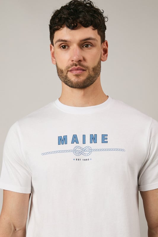 Soft jersey cotton t-shirt featuring the distinctive Maine rope graphic print
        Classic crew neckline with ribbed trim for a comfortable fit
        Short sleeves with clean-finished edges for everyday comfort
        Relaxed yet structured silhouette that maintains its shape throughout the day
        Versatile design that pairs effortlessly with both casual and smart-casual attire
    
    This Maine graphic t-shirt combines simplicity with subtle nautical flair, making it a wardrobe essential for the modern gent. The distinctive rope design adds character without overwhelming, perfect for those who appreciate understated style. Pair with dark chino shorts and trainers as shown for a refined summer look, or layer under an unstructured blazer with tailored trousers for smart-casual occasions. The breathable cotton fabric ensures all-day comfort whether you're meeting friends for a weekend brunch or enjoying a casual evening at the local pub. This t-shirt transitions seamlessly from daytime errands to relaxed evening gatherings, embodying that effortless British casual style that never feels overdone.