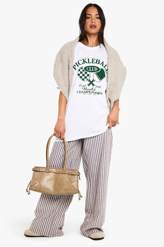 Oversized fit for ultimate comfort and relaxed styling
        Bold Pickleball Club graphic print with retro sports appeal
        Short sleeves with dropped shoulders for a contemporary silhouette
        Soft cotton fabric that's gentle against the skin
        Versatile crew neckline that works with multiple styling options
    
    Make a statement with this trendy oversized Pickleball t-shirt that perfectly balances sporty charm with laid-back cool. The roomy silhouette offers effortless styling potential - pair with striped wide-leg trousers as shown for a contemporary casual look, or team with cycling shorts and trainers for an on-trend athleisure ensemble. Layer under an open shirt or cardigan for cooler days, or simply throw on with your favourite denim and canvas trainers for weekend brunches. This conversation-starting tee works brilliantly for casual gatherings, coffee dates, or relaxed family events. The versatile design allows for customisation with accessories - add a crossbody bag and cap for daytime outings or dress up with statement jewellery and a leather jacket for evening casual wear. A must-have addition to your everyday wardrobe rotation.