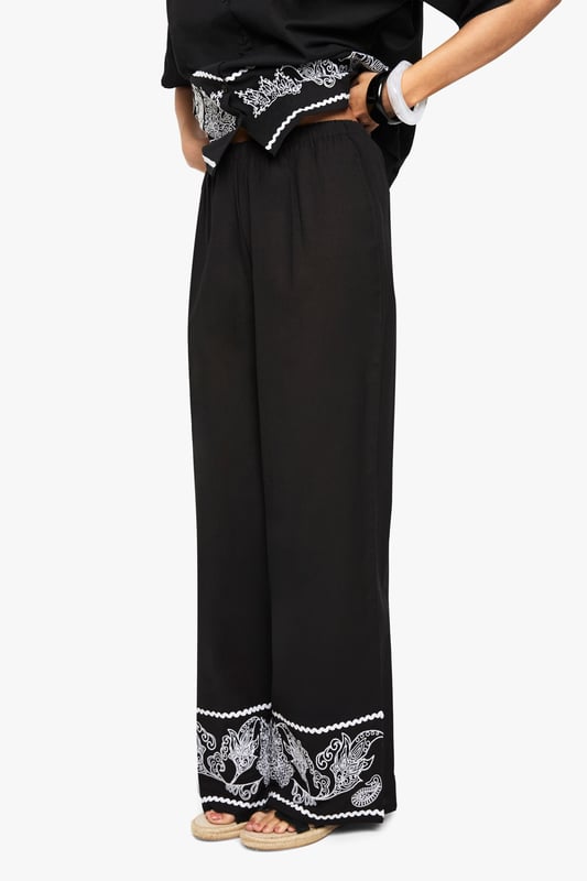 Cotton poplin wide leg trousers featuring striking embroidered border detail
        Relaxed silhouette with comfortable high-rise waistband
        Matching embroidered short-sleeve shirt creates a coordinated set
        Breathable cotton fabric ideal for warm-weather styling
        Versatile wide leg cut that flatters all body shapes
    
    Make a statement in these eye-catching embroidered wide leg trousers from Boohoo. The striking contrast border detailing adds artistic flair to this casual yet sophisticated piece. Crafted from breathable cotton poplin, these trousers offer both comfort and style for your everyday wardrobe. Style them as shown with the matching embroidered shirt for a coordinated look that's perfect for summer gatherings, or pair with a simple vest top and trainers for a more relaxed daytime ensemble. The wide leg silhouette creates a breezy, effortless feel that works brilliantly with flat sandals as pictured. For cooler evenings, layer with a denim jacket and accessorise with a woven bag to complete this contemporary casual look. These trousers transition seamlessly from beach holidays to city breaks, offering versatility for the fashion-forward woman.