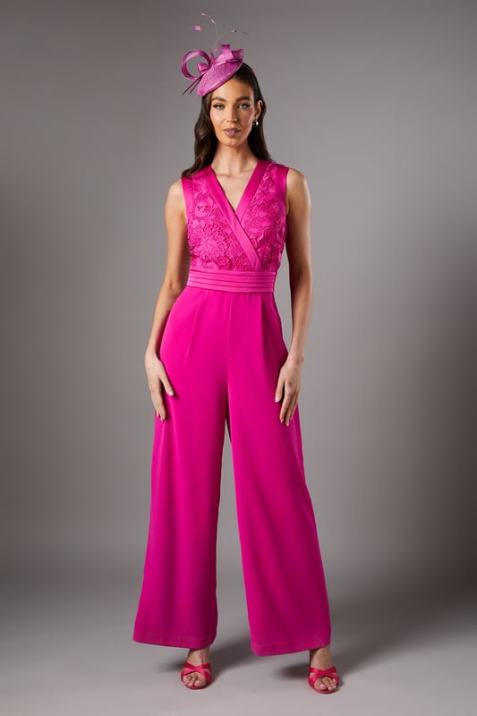 Elegant lace bodice with intricate detailing across the wrap-style V neckline
        Flattering pleated waistband that accentuates the silhouette
        Sleeveless design perfect for sophisticated occasion wear
        Flowing wide-leg trousers that create a graceful movement
        Refined crepe fabric that drapes beautifully for all-day comfort
    
    Make a striking entrance at your next special occasion with this sophisticated Coast jumpsuit. The delicate lace bodice creates a textural contrast against the smooth crepe wide-leg trousers, whilst the wrap-style V neckline frames the dcolletage beautifully. Style as shown with a coordinating fascinator and statement earrings for race day elegance, or pair with metallic heels and a clutch bag for wedding guest perfection. The wide-leg silhouette offers both comfort and a dramatic flair as you move, making this jumpsuit a standout alternative to a traditional dress. For cooler evenings, layer with a tailored blazer or delicate pashmina to maintain the refined aesthetic whilst adding practicality to your ensemble.