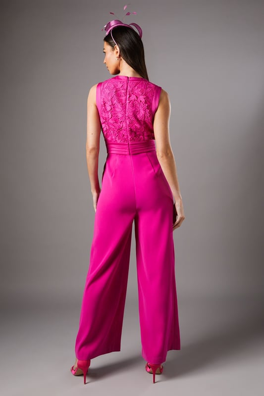 Elegant lace bodice with intricate detailing across the wrap-style V neckline
        Flattering pleated waistband that accentuates the silhouette
        Sleeveless design perfect for sophisticated occasion wear
        Flowing wide-leg trousers that create a graceful movement
        Refined crepe fabric that drapes beautifully for all-day comfort
    
    Make a striking entrance at your next special occasion with this sophisticated Coast jumpsuit. The delicate lace bodice creates a textural contrast against the smooth crepe wide-leg trousers, whilst the wrap-style V neckline frames the dcolletage beautifully. Style as shown with a coordinating fascinator and statement earrings for race day elegance, or pair with metallic heels and a clutch bag for wedding guest perfection. The wide-leg silhouette offers both comfort and a dramatic flair as you move, making this jumpsuit a standout alternative to a traditional dress. For cooler evenings, layer with a tailored blazer or delicate pashmina to maintain the refined aesthetic whilst adding practicality to your ensemble.