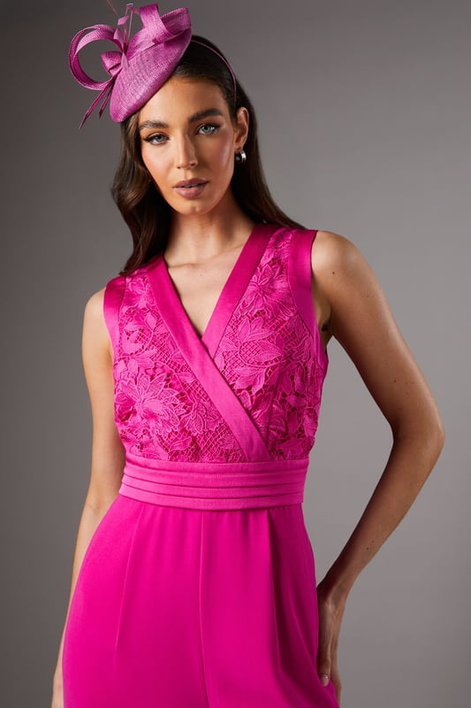 Elegant lace bodice with intricate detailing across the wrap-style V neckline
        Flattering pleated waistband that accentuates the silhouette
        Sleeveless design perfect for sophisticated occasion wear
        Flowing wide-leg trousers that create a graceful movement
        Refined crepe fabric that drapes beautifully for all-day comfort
    
    Make a striking entrance at your next special occasion with this sophisticated Coast jumpsuit. The delicate lace bodice creates a textural contrast against the smooth crepe wide-leg trousers, whilst the wrap-style V neckline frames the dcolletage beautifully. Style as shown with a coordinating fascinator and statement earrings for race day elegance, or pair with metallic heels and a clutch bag for wedding guest perfection. The wide-leg silhouette offers both comfort and a dramatic flair as you move, making this jumpsuit a standout alternative to a traditional dress. For cooler evenings, layer with a tailored blazer or delicate pashmina to maintain the refined aesthetic whilst adding practicality to your ensemble.