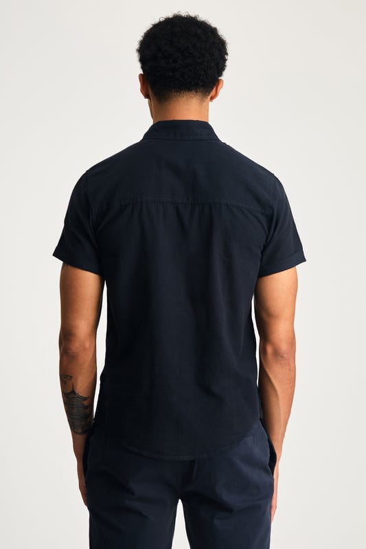 This short sleeve cotton-linen mix shirt by Nines features a sleek embroidered logo on the chest. Lightweight and breathable, it’s perfect for warm days. A stylish and comfortable addition to your wardrobe, offering the ideal balance of relaxed yet refined style.