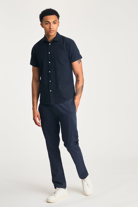 This short sleeve cotton-linen mix shirt by Nines features a sleek embroidered logo on the chest. Lightweight and breathable, it’s perfect for warm days. A stylish and comfortable addition to your wardrobe, offering the ideal balance of relaxed yet refined style.