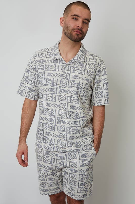 Freshen up your summer wardrobe with this tribal print relaxed fit shirt from Threadbare. This short sleeve printed shirt cut in a relaxed fit is an essential for bringing a bit of style to your outfit. Made from a textured fabric and finished with a revere style collar and button through fastening. Team in the daytime with denim shorts, or smarten up with a pair of chino shorts.