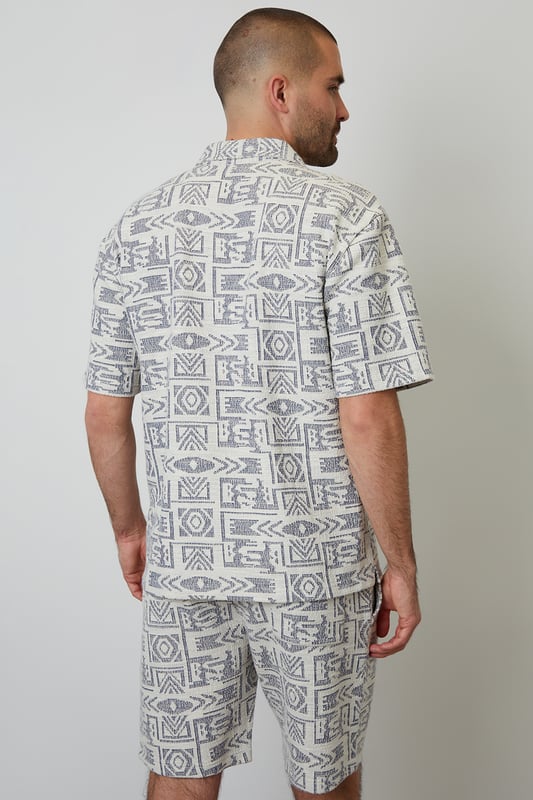 Freshen up your summer wardrobe with this tribal print relaxed fit shirt from Threadbare. This short sleeve printed shirt cut in a relaxed fit is an essential for bringing a bit of style to your outfit. Made from a textured fabric and finished with a revere style collar and button through fastening. Team in the daytime with denim shorts, or smarten up with a pair of chino shorts.