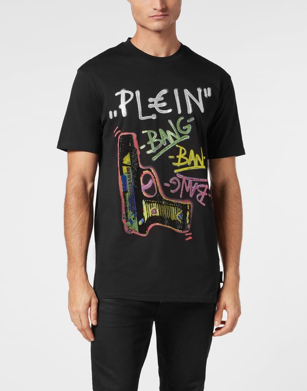 Dit grafische T-shirt is ongegeneerd brutaal en straalt rauwe energie uit met op graffiti geïnspireerd artwork en de kenmerkende kristallen details. Een onverschrokken fusie van kunst, attitude en luxe vakmanschap.    Past het best bij cargos of onder oversized bovenkleding Premium katoenen constructie met een zachte, gestructureerde hand Hand aangebrachte kristallen verheffen de street-art graphic Graffiti-belettering en geweermotief voor maximale visuele impact Een opvallend stuk dat edgy, high-end streetwear definieert