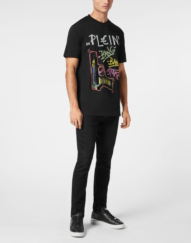 Dit grafische T-shirt is ongegeneerd brutaal en straalt rauwe energie uit met op graffiti geïnspireerd artwork en de kenmerkende kristallen details. Een onverschrokken fusie van kunst, attitude en luxe vakmanschap.    Past het best bij cargos of onder oversized bovenkleding Premium katoenen constructie met een zachte, gestructureerde hand Hand aangebrachte kristallen verheffen de street-art graphic Graffiti-belettering en geweermotief voor maximale visuele impact Een opvallend stuk dat edgy, high-end streetwear definieert