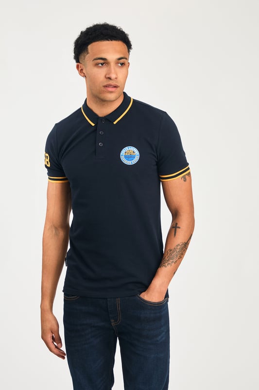 Navy Cotton Short Sleeve Button-Up Polo Shirt This Tokyo Laundry polo shirt features a cotton pique blend for comfort and breathability. With a stylish logo badge on the chest, tipping under the collar, and a unique sleeve print, it combines modern design and quality for a versatile, casual look. Perfect for everyday wear.