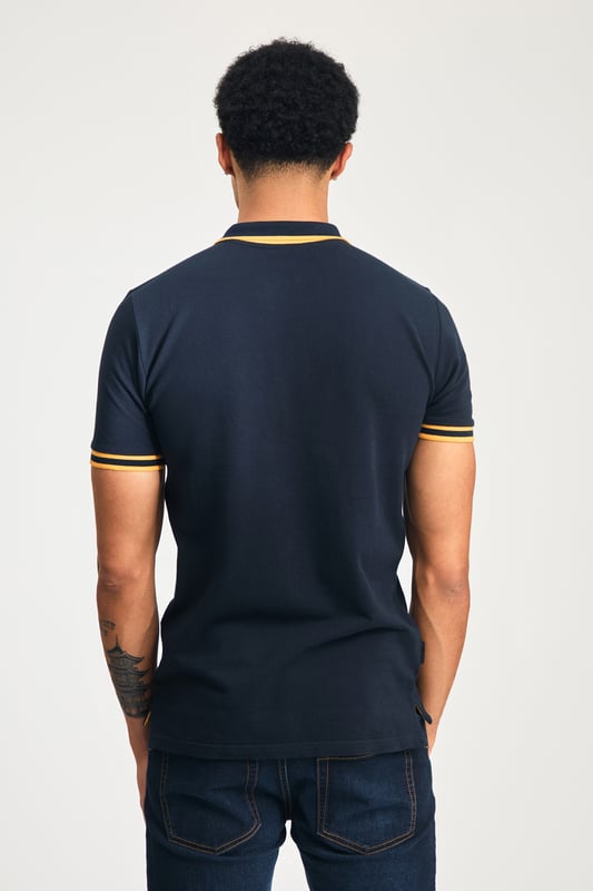 Navy Cotton Short Sleeve Button-Up Polo Shirt This Tokyo Laundry polo shirt features a cotton pique blend for comfort and breathability. With a stylish logo badge on the chest, tipping under the collar, and a unique sleeve print, it combines modern design and quality for a versatile, casual look. Perfect for everyday wear.