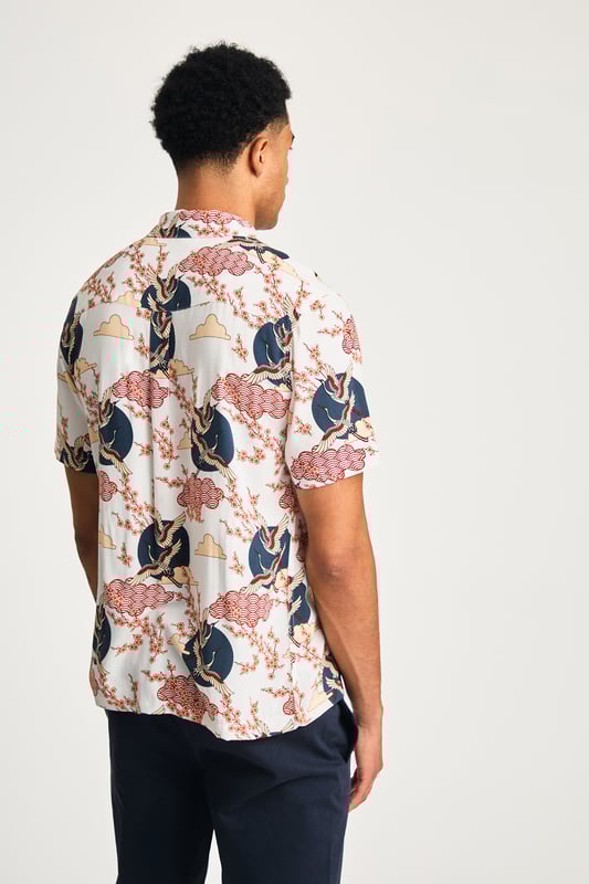 This resort-style shirt by Nines features a cool eagle and blossom print, adding a stylish look to your summer wardrobe. Lightweight and breathable, it's perfect for holidays or sunny days. A standout piece that effortlessly combines comfort and style for a laid-back, eye-catching look.
