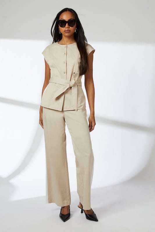 Elegant button-front waistcoat with distinctive round buttons for a refined finish
        Flattering cap sleeves that create a clean, contemporary silhouette
        Self-tie belt that cinches the waist for a customised fit
        Collarless neckline offering a modern, minimalist aesthetic
        Regular fit design ensuring comfortable all-day wear
    
    This versatile Principles waistcoat brings sophisticated structure to your daywear collection. The clean lines and button detailing create a polished look that works beautifully for various casual occasions. Style it as shown with matching wide-leg trousers for an effortlessly coordinated ensemble, or break it up with slim-fit denim and trainers for a more relaxed approach. The adjustable belt allows you to create definition at the waist, making it flattering for all body types. Perfect for family gatherings, brunch dates or gallery visits, this piece transitions seamlessly from day to evening when paired with statement jewellery and sleek mules. The breathable lyocell-cotton blend ensures comfort throughout the day, while the timeless design promises to remain a wardrobe staple for seasons to come.