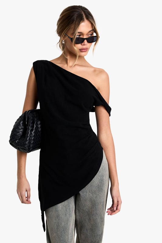 Striking one-shoulder design with elegant draping detail
        Asymmetric hemline creates a contemporary silhouette
        Soft linen-blend fabric offers comfort with a refined finish
        Versatile piece that transitions effortlessly from day to evening
        Flattering fit that accentuates the shoulder and dcolletage
    
    Make a statement with this beautifully draped one-shoulder top that combines contemporary design with effortless style. The asymmetric neckline and hemline create visual interest whilst the linen-blend fabric ensures comfort throughout the day. Style with relaxed trousers as seen on our model for a balanced silhouette that works perfectly for casual gatherings or weekend brunches. For evening occasions, pair with tailored trousers and statement earrings. Add a structured clutch and strappy heels to transform this versatile piece into an outfit worthy of dinner dates or gallery openings. The draped detail adds movement and dimension, making this top a standout addition to your wardrobe that can be styled in multiple ways across seasons.