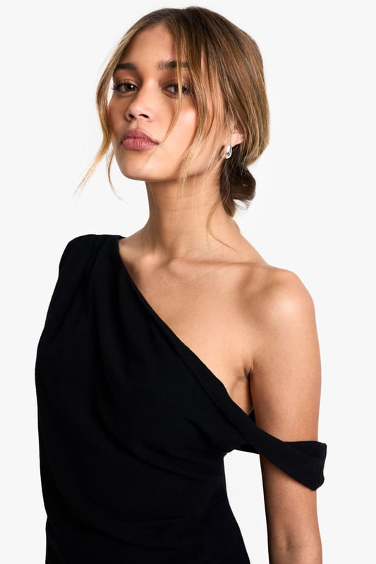 Striking one-shoulder design with elegant draping detail
        Asymmetric hemline creates a contemporary silhouette
        Soft linen-blend fabric offers comfort with a refined finish
        Versatile piece that transitions effortlessly from day to evening
        Flattering fit that accentuates the shoulder and dcolletage
    
    Make a statement with this beautifully draped one-shoulder top that combines contemporary design with effortless style. The asymmetric neckline and hemline create visual interest whilst the linen-blend fabric ensures comfort throughout the day. Style with relaxed trousers as seen on our model for a balanced silhouette that works perfectly for casual gatherings or weekend brunches. For evening occasions, pair with tailored trousers and statement earrings. Add a structured clutch and strappy heels to transform this versatile piece into an outfit worthy of dinner dates or gallery openings. The draped detail adds movement and dimension, making this top a standout addition to your wardrobe that can be styled in multiple ways across seasons.