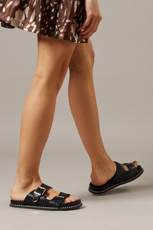 Distinctive double buckle design for adjustable fit and contemporary appeal
        Cushioned footbed provides exceptional comfort for all-day wear
        Flat heel measuring between 0-2cm offers practical stability
        Faux leather construction delivers a polished finish with durability
        Versatile neutral tone complements a wide range of summer outfits
    
    These Faith Gianne sliders combine practicality with effortless style for your warm-weather wardrobe. The double buckle detail adds a contemporary twist to a classic footbed design, making them a standout choice for casual daywear. Pair them with a flowing summer dress as shown for a relaxed yet put-together look, or style with cropped trousers and a linen shirt for weekend brunches. The flat heel ensures comfort during family gatherings or leisurely strolls through town, while the sturdy construction means they'll withstand regular wear throughout the season. These sliders transition seamlessly from garden parties to beachside cafs, offering versatility without compromising on style. Their understated design makes them an excellent foundation piece for building numerous summer ensembles, whether you're dressing for a casual lunch or a day of sightseeing.