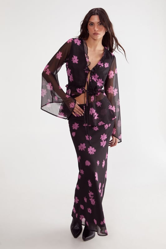 Lightweight chiffon fabric with all-over ditsy floral print
        Elegant tie-front closure with ruffle detailing
        Dramatic fluted sleeves for statement appeal
        Feminine V-neckline with subtle ruffle trim
        Semi-sheer finish for layered styling versatility
    
    This enchanting Nasty Gal top showcases the perfect balance between bohemian flair and contemporary chic. The delicate chiffon construction creates a floaty silhouette, while the distinctive fluted sleeves add dramatic movement to your ensemble. Style with high-waisted trousers and strappy heels for an evening soire, or pair with your favourite denim and ankle boots for a more casual approach. The tie-front detail allows for adjustable styling, making this piece wonderfully adaptable for various occasions. For office wear, layer with a fitted camisole underneath and team with tailored trousers for a look that transitions seamlessly from desk to dinner. The ruffle detailing adds a touch of romance, perfect for date nights or special gatherings where you want to make a subtle yet sophisticated statement.