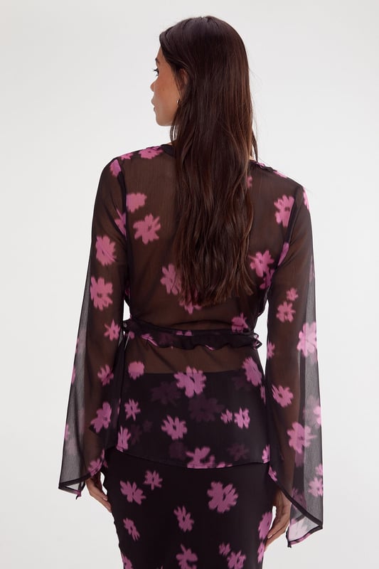 Lightweight chiffon fabric with all-over ditsy floral print
        Elegant tie-front closure with ruffle detailing
        Dramatic fluted sleeves for statement appeal
        Feminine V-neckline with subtle ruffle trim
        Semi-sheer finish for layered styling versatility
    
    This enchanting Nasty Gal top showcases the perfect balance between bohemian flair and contemporary chic. The delicate chiffon construction creates a floaty silhouette, while the distinctive fluted sleeves add dramatic movement to your ensemble. Style with high-waisted trousers and strappy heels for an evening soire, or pair with your favourite denim and ankle boots for a more casual approach. The tie-front detail allows for adjustable styling, making this piece wonderfully adaptable for various occasions. For office wear, layer with a fitted camisole underneath and team with tailored trousers for a look that transitions seamlessly from desk to dinner. The ruffle detailing adds a touch of romance, perfect for date nights or special gatherings where you want to make a subtle yet sophisticated statement.