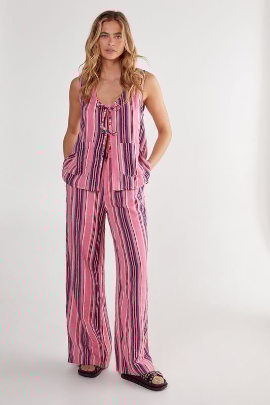 Sleeveless vest with eye-catching vertical stripe pattern
        Distinctive tie-front detail with multiple closures for adjustable styling
        Scoop neckline offering a flattering silhouette
        Practical dual front pockets for convenience
        Relaxed fit with slightly longer back hem for versatile coverage
    
    This striking Nasty Gal vest brings playful charm to your casual wardrobe. The tie-front design creates a customisable fit that works beautifully whether worn loose or secured for a more defined shape. Style with the matching striped trousers as seen on our model for a coordinated set that makes a statement, or break it up with your favourite denim shorts for a more relaxed approach. The lightweight cotton fabric makes this piece perfect for warm-weather gatherings, weekend brunches or casual garden parties. Layer under a denim jacket when temperatures drop, or throw on with trainers for an effortlessly cool daytime look. The versatile design transitions seamlessly from beach cover-up to family barbecue attire, making it an essential addition to your summer capsule wardrobe.