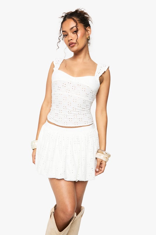 Sleeveless broderie anglaise top with intricate eyelet detailing throughout
        Feminine sweetheart neckline for a flattering silhouette
        Delicate flutter cap sleeves adding a touch of romance
        Figure-hugging fit with slight stretch for comfort
        Cropped length perfect for pairing with high-waisted bottoms
    
    This charming broderie anglaise top captures the essence of carefree summer style with its delicate eyelet pattern and feminine details. The sweet flutter sleeves and sweetheart neckline create a soft, romantic look that's perfect for warm-weather occasions. Style it as shown with a matching broderie mini skirt and western boots for a festival-ready ensemble that balances bohemian flair with contemporary edge. For a more relaxed daytime look, pair with your favourite denim shorts and trainers. This versatile piece transitions effortlessly from casual brunches to family barbecues, and can be dressed up with tailored trousers and ballet flats for garden parties. Add layered bangles and hoop earrings to complete this effortlessly chic Boohoo look.