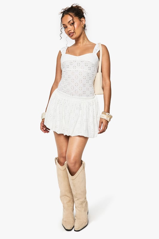Sleeveless broderie anglaise top with intricate eyelet detailing throughout
        Feminine sweetheart neckline for a flattering silhouette
        Delicate flutter cap sleeves adding a touch of romance
        Figure-hugging fit with slight stretch for comfort
        Cropped length perfect for pairing with high-waisted bottoms
    
    This charming broderie anglaise top captures the essence of carefree summer style with its delicate eyelet pattern and feminine details. The sweet flutter sleeves and sweetheart neckline create a soft, romantic look that's perfect for warm-weather occasions. Style it as shown with a matching broderie mini skirt and western boots for a festival-ready ensemble that balances bohemian flair with contemporary edge. For a more relaxed daytime look, pair with your favourite denim shorts and trainers. This versatile piece transitions effortlessly from casual brunches to family barbecues, and can be dressed up with tailored trousers and ballet flats for garden parties. Add layered bangles and hoop earrings to complete this effortlessly chic Boohoo look.