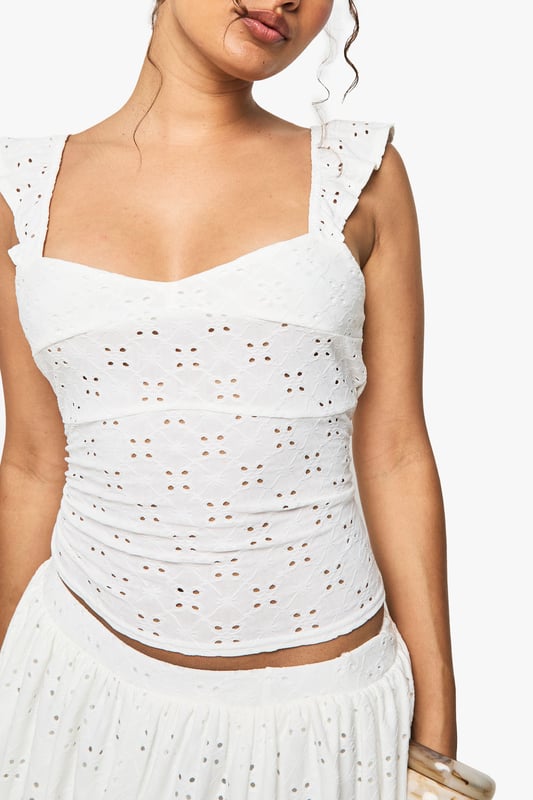 Sleeveless broderie anglaise top with intricate eyelet detailing throughout
        Feminine sweetheart neckline for a flattering silhouette
        Delicate flutter cap sleeves adding a touch of romance
        Figure-hugging fit with slight stretch for comfort
        Cropped length perfect for pairing with high-waisted bottoms
    
    This charming broderie anglaise top captures the essence of carefree summer style with its delicate eyelet pattern and feminine details. The sweet flutter sleeves and sweetheart neckline create a soft, romantic look that's perfect for warm-weather occasions. Style it as shown with a matching broderie mini skirt and western boots for a festival-ready ensemble that balances bohemian flair with contemporary edge. For a more relaxed daytime look, pair with your favourite denim shorts and trainers. This versatile piece transitions effortlessly from casual brunches to family barbecues, and can be dressed up with tailored trousers and ballet flats for garden parties. Add layered bangles and hoop earrings to complete this effortlessly chic Boohoo look.