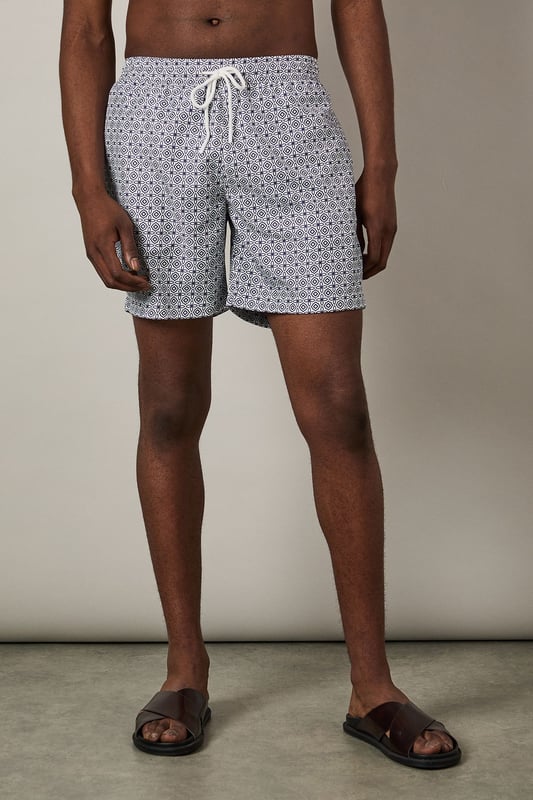 Classic mid-length swim shorts with all-over geometric print
        Comfortable adjustable drawstring waist for the perfect fit
        Quick-drying woven fabric ideal for beach and poolside wear
        Side pockets for convenient storage of small essentials
        Relaxed fit design offering ease of movement during activities
    
    These Burton swim shorts combine practicality with understated style for the modern man who values both comfort and classic design. The distinctive geometric print adds visual interest without being overly bold, making these shorts versatile enough for various summer settings. Pair with a plain white t-shirt and casual shirt as shown for a relaxed beachside lunch, or simply throw on with your favourite sunglasses and flip-flops for a day by the pool. The adjustable waist ensures all-day comfort whether you're swimming, playing beach volleyball, or enjoying a casual barbecue with mates. These shorts transition effortlessly from daytime water activities to evening drinks at a beachfront bar, making them an essential addition to your holiday wardrobe and weekend outings throughout the summer months.