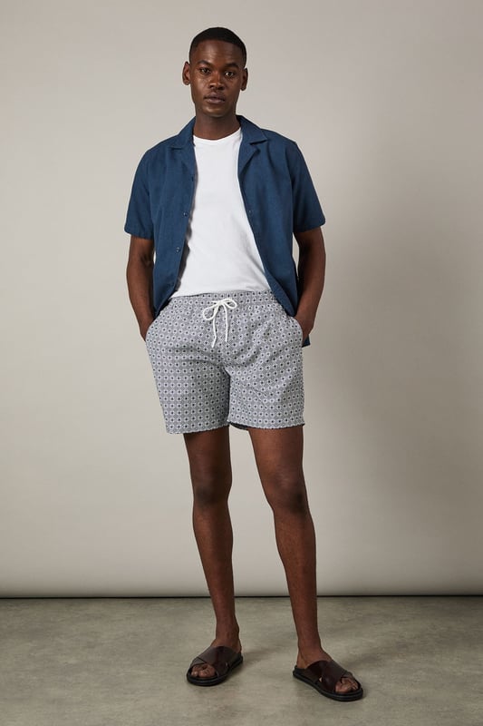 Classic mid-length swim shorts with all-over geometric print
        Comfortable adjustable drawstring waist for the perfect fit
        Quick-drying woven fabric ideal for beach and poolside wear
        Side pockets for convenient storage of small essentials
        Relaxed fit design offering ease of movement during activities
    
    These Burton swim shorts combine practicality with understated style for the modern man who values both comfort and classic design. The distinctive geometric print adds visual interest without being overly bold, making these shorts versatile enough for various summer settings. Pair with a plain white t-shirt and casual shirt as shown for a relaxed beachside lunch, or simply throw on with your favourite sunglasses and flip-flops for a day by the pool. The adjustable waist ensures all-day comfort whether you're swimming, playing beach volleyball, or enjoying a casual barbecue with mates. These shorts transition effortlessly from daytime water activities to evening drinks at a beachfront bar, making them an essential addition to your holiday wardrobe and weekend outings throughout the summer months.