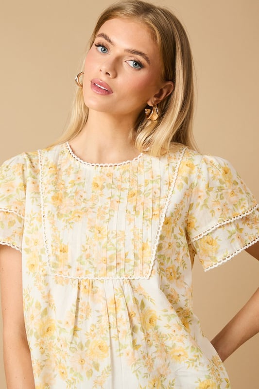 Charming crew neck blouse with delicate frill shoulder detail for a feminine touch
        Elegant pintuck detailing on the front bodice creates subtle texture and visual interest
        Dainty floral print throughout with a soft, romantic aesthetic
        Fluttery short sleeves with pretty trim detailing for added dimension
        Relaxed silhouette with a subtle empire waist for a flattering, comfortable fit
    
    This enchanting Oasis blouse combines classic femininity with contemporary styling. The delicate frill shoulders and pintuck detailing create a wonderfully romantic silhouette that's perfect for everyday wear. Style with relaxed denim jeans and flat sandals for casual weekend brunches, or pair with tailored trousers and ballet flats for a polished office look. The versatile design transitions beautifully from day to evening - simply swap your daytime accessories for statement earrings and a clutch bag for dinner with friends. The blouse's relaxed fit ensures all-day comfort whilst maintaining a put-together appearance, making it an ideal choice for family gatherings or casual meetups. This charming piece captures Oasis's signature feminine aesthetic whilst offering practical versatility for your everyday wardrobe.