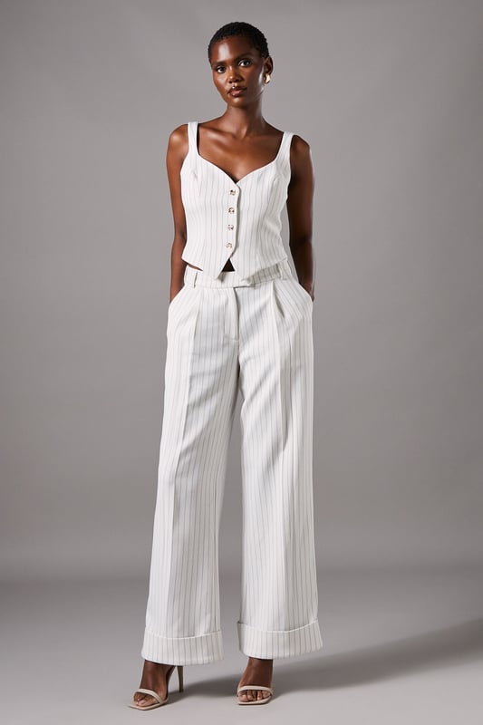Elegant strappy waistcoat featuring a sophisticated pinstripe pattern
        Flattering V-neckline complemented by wide shoulder straps for comfort
        Decorative button-through front with contrasting metallic buttons
        Tailored fit with a slight stretch for a figure-enhancing silhouette
        Versatile cropped length perfect for pairing with high-waisted bottoms
    
    This refined Coast waistcoat brings contemporary sophistication to occasion dressing. The classic pinstripe pattern is reimagined with a feminine twist through the strappy design and fitted silhouette. Style with the matching wide-leg trousers as seen on our model for an impeccably coordinated ensemble that commands attention at summer weddings or race day events. For evening occasions, pair with a sleek pencil skirt and delicate jewellery for a look that conveys understated elegance. The crepe fabric offers comfortable wear throughout the day while maintaining its structured shape. This versatile piece transitions beautifully from formal daytime events to evening soires with just a change of accessories - try statement earrings and a clutch bag to transform your look as day turns to night.