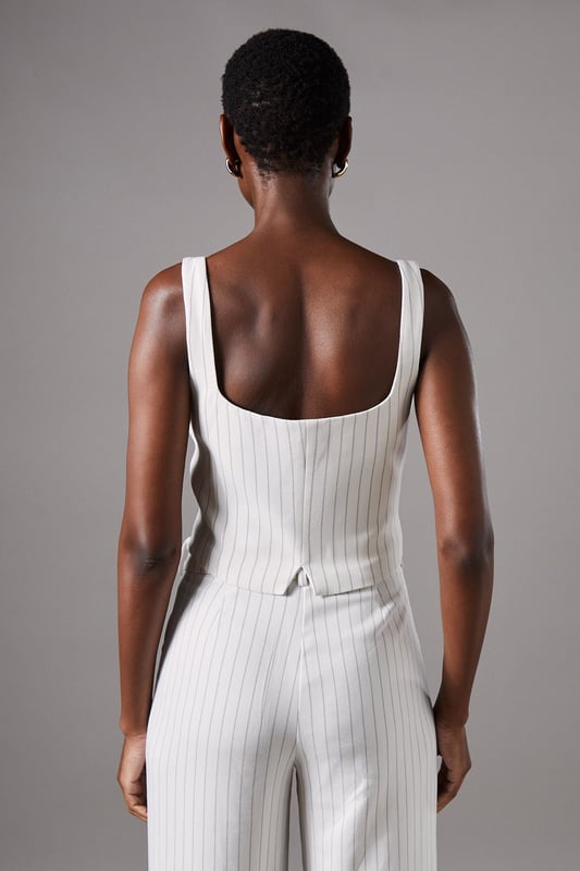 Elegant strappy waistcoat featuring a sophisticated pinstripe pattern
        Flattering V-neckline complemented by wide shoulder straps for comfort
        Decorative button-through front with contrasting metallic buttons
        Tailored fit with a slight stretch for a figure-enhancing silhouette
        Versatile cropped length perfect for pairing with high-waisted bottoms
    
    This refined Coast waistcoat brings contemporary sophistication to occasion dressing. The classic pinstripe pattern is reimagined with a feminine twist through the strappy design and fitted silhouette. Style with the matching wide-leg trousers as seen on our model for an impeccably coordinated ensemble that commands attention at summer weddings or race day events. For evening occasions, pair with a sleek pencil skirt and delicate jewellery for a look that conveys understated elegance. The crepe fabric offers comfortable wear throughout the day while maintaining its structured shape. This versatile piece transitions beautifully from formal daytime events to evening soires with just a change of accessories - try statement earrings and a clutch bag to transform your look as day turns to night.