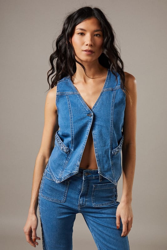 Boxy fit denim waistcoat with distinctive button front closure
        Sleeveless design with V-neckline for a feminine silhouette
        Contrast topstitching detail highlighting the structured seams
        Practical front pockets with decorative stitching
        Versatile co-ord piece that can be styled separately or as a set
    
    This Button Front Denim Waistcoat from Warehouse offers effortless edge to your casual wardrobe. The boxy silhouette creates a contemporary shape that pairs brilliantly with the matching flared trousers as seen on our model, or can be styled with your favourite denim jeans for a double denim moment. For daytime outings, layer over a simple white tee and finish with trainers and statement jewellery. When the evening calls, wear it unbuttoned over a fitted bodysuit and team with heeled boots for a touch of after-dark confidence. Perfect for festivals, weekend brunches or casual gatherings, this versatile waistcoat transitions seamlessly through the seasons - simply add layers underneath when temperatures drop. The cotton fabric ensures comfort whilst maintaining that structured denim look that never goes out of style.