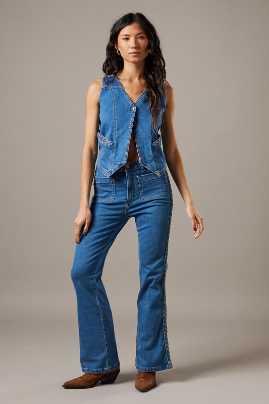 Boxy fit denim waistcoat with distinctive button front closure
        Sleeveless design with V-neckline for a feminine silhouette
        Contrast topstitching detail highlighting the structured seams
        Practical front pockets with decorative stitching
        Versatile co-ord piece that can be styled separately or as a set
    
    This Button Front Denim Waistcoat from Warehouse offers effortless edge to your casual wardrobe. The boxy silhouette creates a contemporary shape that pairs brilliantly with the matching flared trousers as seen on our model, or can be styled with your favourite denim jeans for a double denim moment. For daytime outings, layer over a simple white tee and finish with trainers and statement jewellery. When the evening calls, wear it unbuttoned over a fitted bodysuit and team with heeled boots for a touch of after-dark confidence. Perfect for festivals, weekend brunches or casual gatherings, this versatile waistcoat transitions seamlessly through the seasons - simply add layers underneath when temperatures drop. The cotton fabric ensures comfort whilst maintaining that structured denim look that never goes out of style.
