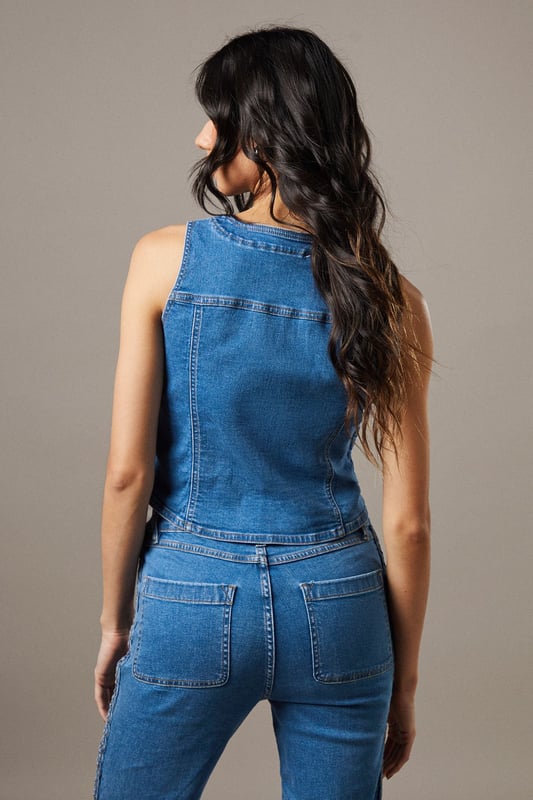 Boxy fit denim waistcoat with distinctive button front closure
        Sleeveless design with V-neckline for a feminine silhouette
        Contrast topstitching detail highlighting the structured seams
        Practical front pockets with decorative stitching
        Versatile co-ord piece that can be styled separately or as a set
    
    This Button Front Denim Waistcoat from Warehouse offers effortless edge to your casual wardrobe. The boxy silhouette creates a contemporary shape that pairs brilliantly with the matching flared trousers as seen on our model, or can be styled with your favourite denim jeans for a double denim moment. For daytime outings, layer over a simple white tee and finish with trainers and statement jewellery. When the evening calls, wear it unbuttoned over a fitted bodysuit and team with heeled boots for a touch of after-dark confidence. Perfect for festivals, weekend brunches or casual gatherings, this versatile waistcoat transitions seamlessly through the seasons - simply add layers underneath when temperatures drop. The cotton fabric ensures comfort whilst maintaining that structured denim look that never goes out of style.