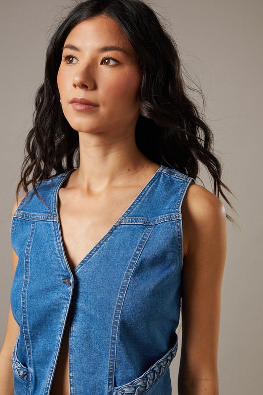 Boxy fit denim waistcoat with distinctive button front closure
        Sleeveless design with V-neckline for a feminine silhouette
        Contrast topstitching detail highlighting the structured seams
        Practical front pockets with decorative stitching
        Versatile co-ord piece that can be styled separately or as a set
    
    This Button Front Denim Waistcoat from Warehouse offers effortless edge to your casual wardrobe. The boxy silhouette creates a contemporary shape that pairs brilliantly with the matching flared trousers as seen on our model, or can be styled with your favourite denim jeans for a double denim moment. For daytime outings, layer over a simple white tee and finish with trainers and statement jewellery. When the evening calls, wear it unbuttoned over a fitted bodysuit and team with heeled boots for a touch of after-dark confidence. Perfect for festivals, weekend brunches or casual gatherings, this versatile waistcoat transitions seamlessly through the seasons - simply add layers underneath when temperatures drop. The cotton fabric ensures comfort whilst maintaining that structured denim look that never goes out of style.