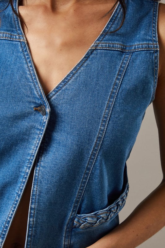 Boxy fit denim waistcoat with distinctive button front closure
        Sleeveless design with V-neckline for a feminine silhouette
        Contrast topstitching detail highlighting the structured seams
        Practical front pockets with decorative stitching
        Versatile co-ord piece that can be styled separately or as a set
    
    This Button Front Denim Waistcoat from Warehouse offers effortless edge to your casual wardrobe. The boxy silhouette creates a contemporary shape that pairs brilliantly with the matching flared trousers as seen on our model, or can be styled with your favourite denim jeans for a double denim moment. For daytime outings, layer over a simple white tee and finish with trainers and statement jewellery. When the evening calls, wear it unbuttoned over a fitted bodysuit and team with heeled boots for a touch of after-dark confidence. Perfect for festivals, weekend brunches or casual gatherings, this versatile waistcoat transitions seamlessly through the seasons - simply add layers underneath when temperatures drop. The cotton fabric ensures comfort whilst maintaining that structured denim look that never goes out of style.