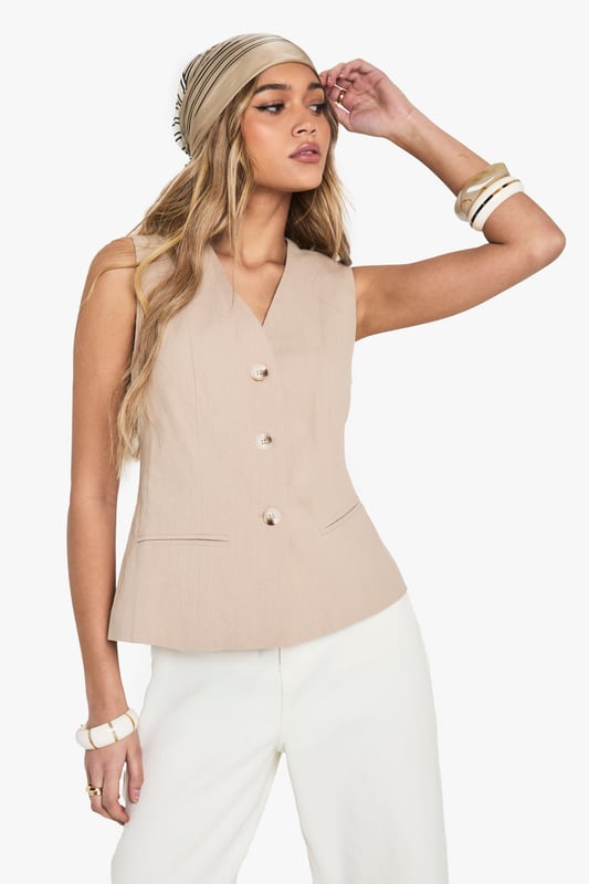 Sleeveless waistcoat with elegant V-neckline for a flattering silhouette
        Linen-look texture adds dimension and visual interest to your outfit
        Structured button-front design with subtle waist definition
        Versatile sleeveless cut perfect for layering or wearing alone
        Clean-lined silhouette with a contemporary tailored finish
    
    This sophisticated waistcoat brings effortless chic to your everyday wardrobe. The linen-look texture creates a relaxed yet refined aesthetic that works brilliantly for various casual occasions. Style with wide-leg trousers as shown for a coordinated ensemble that's perfect for family gatherings or weekend brunches. For cooler days, layer over a fitted long-sleeve top or under a lightweight jacket. Complete the look with a patterned headscarf and stacked bangles for a bohemian touch, or keep it minimal with delicate jewellery for a more understated approach. The neutral tone makes this waistcoat incredibly versatile - pair with denim for an elevated casual look or with tailored pieces for smart-casual events. Machine washable for easy care, this piece combines style with practicality for the fashion-forward woman.