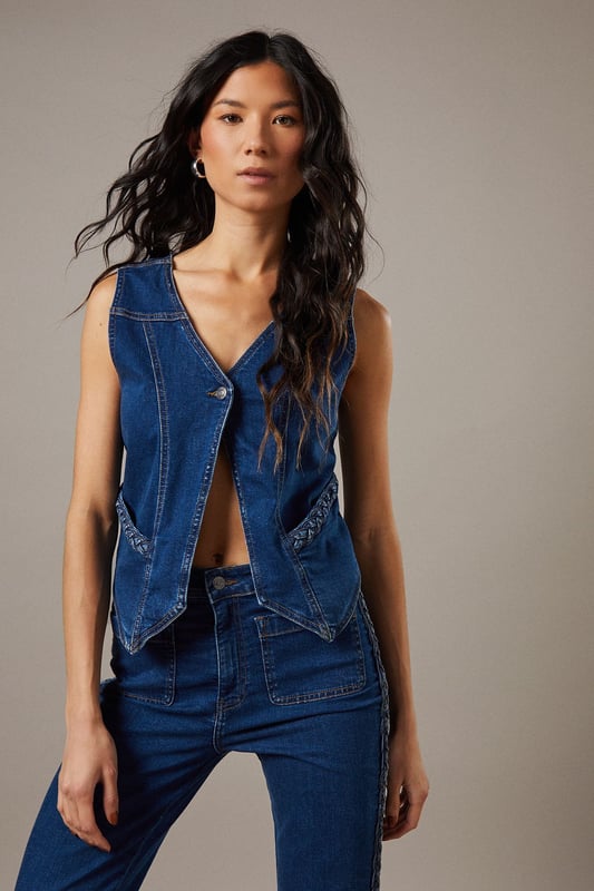 Boxy fit denim waistcoat with distinctive button front closure
        Sleeveless design with V-neckline for a feminine silhouette
        Contrast topstitching detail highlighting the structured seams
        Practical front pockets with decorative stitching
        Versatile co-ord piece that can be styled separately or as a set
    
    This Button Front Denim Waistcoat from Warehouse offers effortless edge to your casual wardrobe. The boxy silhouette creates a contemporary shape that pairs brilliantly with the matching flared trousers as seen on our model, or can be styled with your favourite denim jeans for a double denim moment. For daytime outings, layer over a simple white tee and finish with trainers and statement jewellery. When the evening calls, wear it unbuttoned over a fitted bodysuit and team with heeled boots for a touch of after-dark confidence. Perfect for festivals, weekend brunches or casual gatherings, this versatile waistcoat transitions seamlessly through the seasons - simply add layers underneath when temperatures drop. The cotton fabric ensures comfort whilst maintaining that structured denim look that never goes out of style.