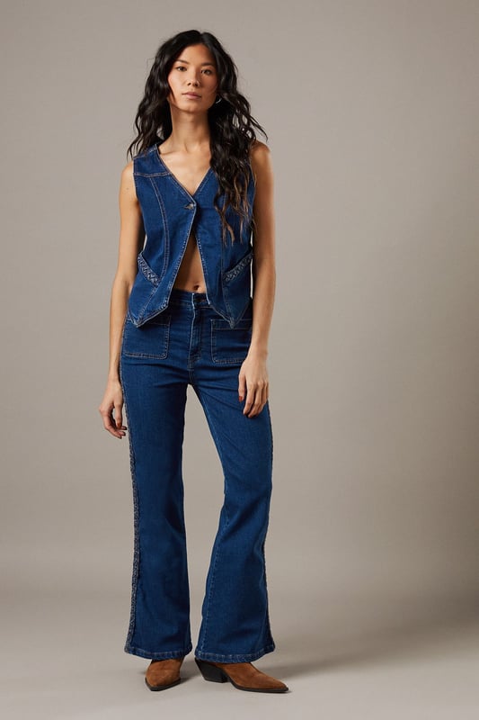 Boxy fit denim waistcoat with distinctive button front closure
        Sleeveless design with V-neckline for a feminine silhouette
        Contrast topstitching detail highlighting the structured seams
        Practical front pockets with decorative stitching
        Versatile co-ord piece that can be styled separately or as a set
    
    This Button Front Denim Waistcoat from Warehouse offers effortless edge to your casual wardrobe. The boxy silhouette creates a contemporary shape that pairs brilliantly with the matching flared trousers as seen on our model, or can be styled with your favourite denim jeans for a double denim moment. For daytime outings, layer over a simple white tee and finish with trainers and statement jewellery. When the evening calls, wear it unbuttoned over a fitted bodysuit and team with heeled boots for a touch of after-dark confidence. Perfect for festivals, weekend brunches or casual gatherings, this versatile waistcoat transitions seamlessly through the seasons - simply add layers underneath when temperatures drop. The cotton fabric ensures comfort whilst maintaining that structured denim look that never goes out of style.