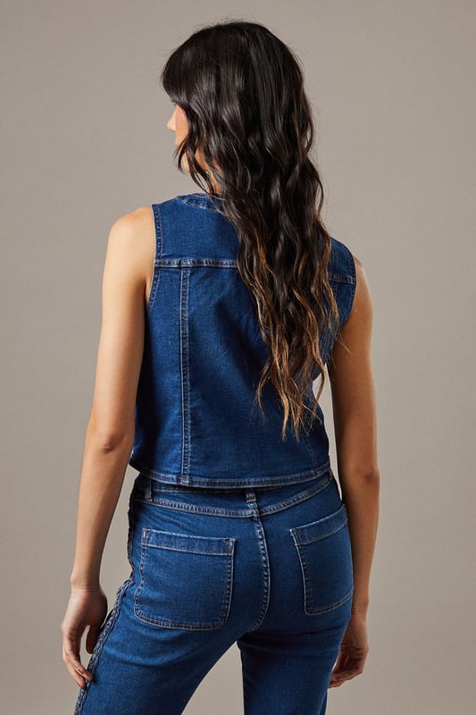 Boxy fit denim waistcoat with distinctive button front closure
        Sleeveless design with V-neckline for a feminine silhouette
        Contrast topstitching detail highlighting the structured seams
        Practical front pockets with decorative stitching
        Versatile co-ord piece that can be styled separately or as a set
    
    This Button Front Denim Waistcoat from Warehouse offers effortless edge to your casual wardrobe. The boxy silhouette creates a contemporary shape that pairs brilliantly with the matching flared trousers as seen on our model, or can be styled with your favourite denim jeans for a double denim moment. For daytime outings, layer over a simple white tee and finish with trainers and statement jewellery. When the evening calls, wear it unbuttoned over a fitted bodysuit and team with heeled boots for a touch of after-dark confidence. Perfect for festivals, weekend brunches or casual gatherings, this versatile waistcoat transitions seamlessly through the seasons - simply add layers underneath when temperatures drop. The cotton fabric ensures comfort whilst maintaining that structured denim look that never goes out of style.