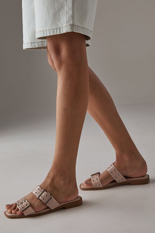 Striking faux patent leather finish that catches the light beautifully
        Distinctive double strap design with eye-catching eyelet and buckle detailing
        Comfortable flat heel measuring between 0-2cm for all-day wearability
        Cushioned footbed providing essential support for extended wear
        Durable synthetic outsole offering reliable grip on various surfaces
    
    These Faith sliders showcase contemporary British style with their statement eyelet and buckle detailing. The gleaming faux patent finish adds a touch of sophistication to even the most casual ensembles. Perfect for warm-weather outings, these versatile flats pair brilliantly with everything from tailored shorts and a ruffled camisole to floaty summer dresses. The practical flat design ensures comfort during family gatherings, weekend brunches, or seaside strolls. Their slip-on style makes them an effortless choice for garden parties or casual shopping trips, while the distinctive hardware elements present a fashion-forward edge that elevates your everyday wardrobe. These sliders transition seamlessly from daytime casual to relaxed evening occasions, making them an essential addition to your summer footwear collection.
